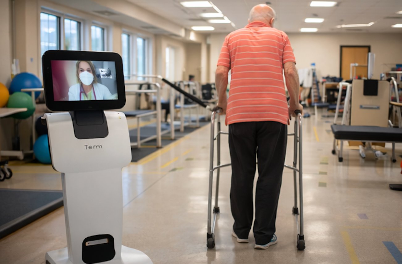 Patient walking with walker alongside telepresence robot in rehab gym